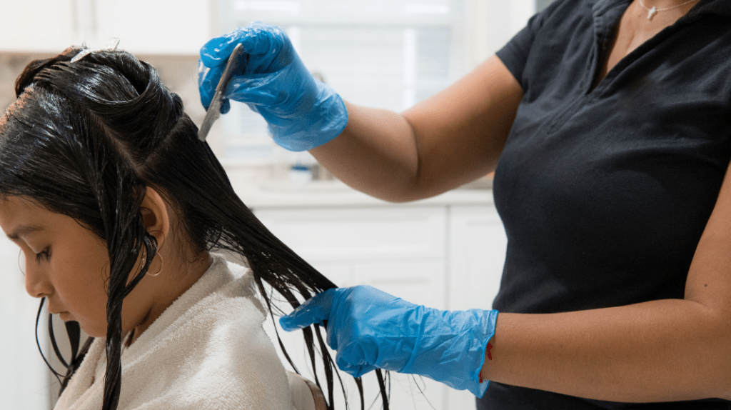 A lice removal technician combs through a child's hair during a home lice treatment